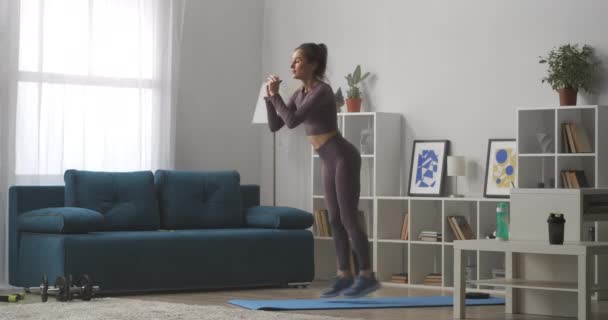 Fitnesstraining zu Hause, junge Frau hockt und springt im Wohnzimmer, sportlicher und aktiver Lebensstil — Stockvideo