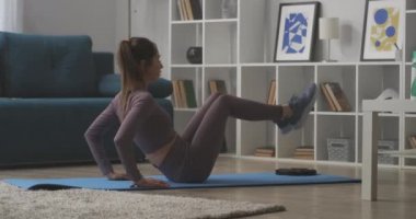 Sportif kadın modern dairenin oturma odasında mekik çekiyor, karantinada eğitim görüyor, sağlıklı bir yaşam tarzı.