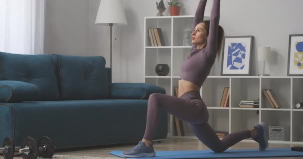 Athletische Frau posiert beim Yoga-Training zu Hause in Kriegerpose, streckt die Hände nach oben, sportlich und gesund — Stockvideo