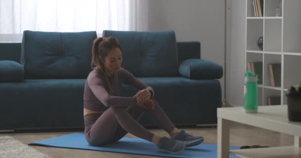 Smukła sportowa kobieta siedzi na podłodze, patrząc na fitness tracker, gadżet dla zdrowego stylu życia, trening w domu — Wideo stockowe