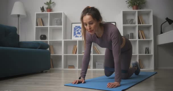 Aerobik i gimnastyka z elastyczną opaską fitness w domu, kobieta stoi na rękach i kolanach, przesuwa nogi na boki — Wideo stockowe