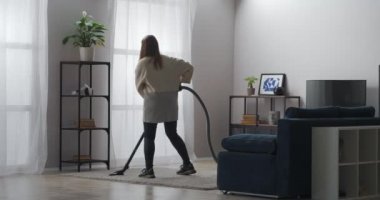 Dans eden kadın apartman dairesinde halı süpürüyor, eğleniyor ve eğleniyor, ev temizliği yapıyor.