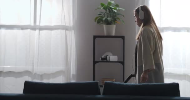 Wanita pirang yang sedang tidur di kamar dan mendengarkan musik dengan headphone, membersihkan rumah pada akhir pekan — Stok Video