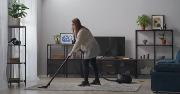 Jovem mulher está usando aspirador de pó na sala de estar, limpeza em casa no fim de semana, dona de casa está fazendo tarefas domésticas — Vídeo de Stock