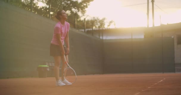 A menina está cansada durante o treinamento de tênis em um campo aberto com uma superfície de sujeira e se inclina em uma raquete. — Vídeo de Stock
