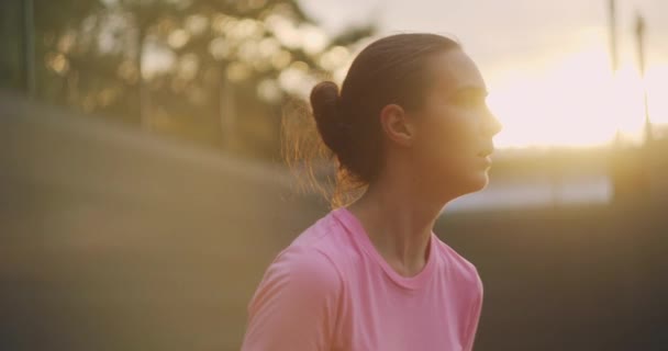 Ein junges Mädchen schlägt in einer Tennispraxis einen Aufschlag mit einer Vorhand. Training bei Sonnenuntergang. Mittlerer Schuss — Stockvideo