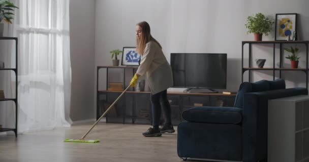 Ibu rumah tangga adalah mencuci lantai di ruang tamu dengan pel, menggunakan sarung tangan karet untuk melindungi tangan, housekeeping — Stok Video