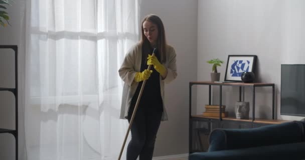Jovem está dançando com esfregona e cantando durante a limpeza de casa no fim de semana na sala de estar — Vídeo de Stock
