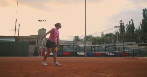 Per l'allenamento di tennis, una ragazza si trova sulla linea di servizio centrale. Sbatte la palla in campo. Servire. Probabile. — Video Stock