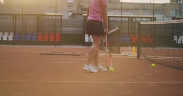 Una joven está cansada después de un intenso entrenamiento de tenis al aire libre. Rolls pelotas de tenis a lo largo de la red. — Vídeo de stock