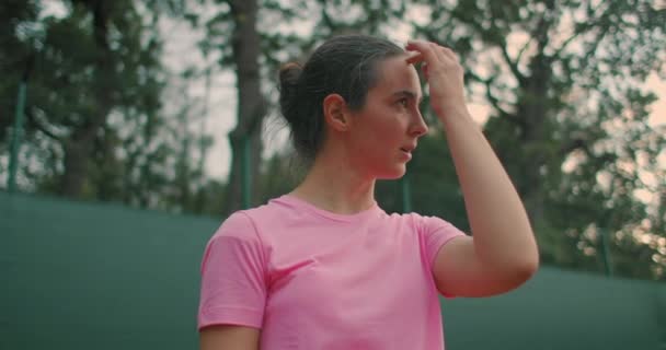 Une fille dans un T-shirt rose avec une raquette de tennis en position prête — Video