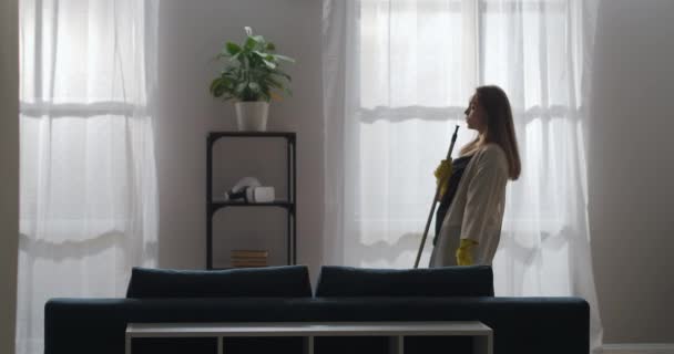 Vrolijke vrouw danst met dweilen en zingen in de woonkamer, schoonmaken van huis en goed humeur, huishoudelijk werk en netheid — Stockvideo