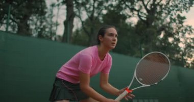 Genç bir kadın gün batımında sert bir tenis kortunda antrenman yapıyor..