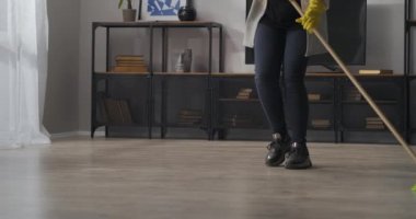 Enerji dolu genç bir kadın odayı paspaslıyor, pozitif dans ediyor, ev hanımının keyfi yerinde, elleri sarı eldivenli.