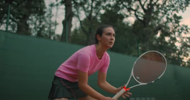 Una giovane donna si allena su un campo da tennis di superficie dura al tramonto la posizione pronta. — Video Stock