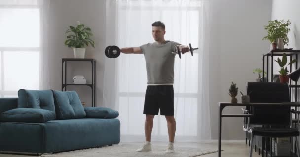 Sportler trainiert mit Kurzhanteln im Wohnzimmer, Fitness zu Hause und gesunder Lebensstil, spannt die Muskeln des Oberkörpers an — Stockvideo