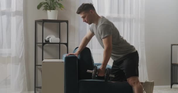 Homem atlético está treinando em apartamento, levantando haltere por um braço, mantendo em forma e musculação, estilo de vida saudável e esportivo — Vídeo de Stock