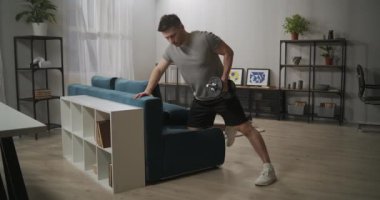 Powerlifter evde dambılla egzersiz yapıyor, oturma odasında kanepeye yaslanıyor, yetişkin sporcu evcil spor salonunda antrenman yapıyor.