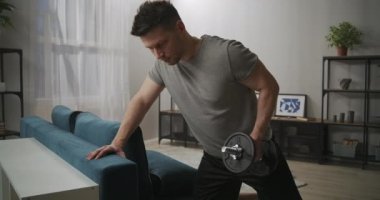 Çekici sporcu adam oturma odasında antrenman yapıyor, ağırlıkla çalışıyor, bir eliyle dambılı kaldırıyor, spor salonunda.