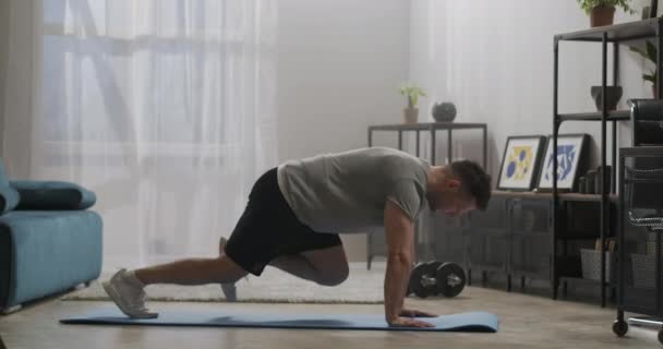 Фитнес-тренировки в гостиной современной квартиры, человек делает упражнения для мышц тела на полу, ногах и руках тренировки — стоковое видео