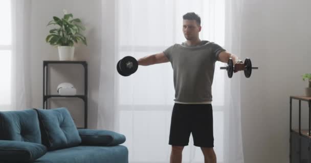 Svalnatý muž trénuje doma, drží činky v rukou a zvedání, posilování a fitness — Stock video