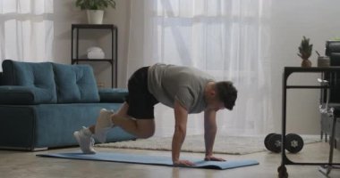 Evde spor salonu, erkek vücut kasları için egzersiz yapıyor, spor paspası ve spor malzemesi kullanarak yerde koşuyor ve yaslanıyor.