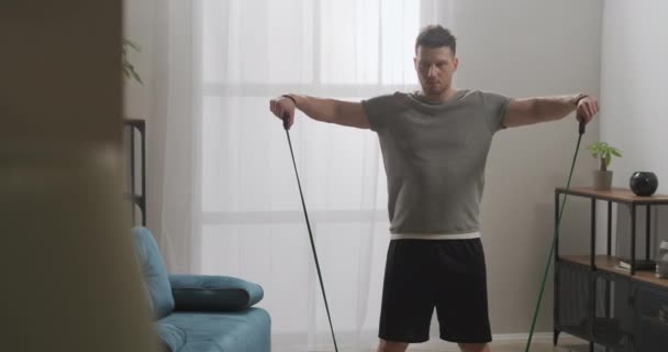 Retrato medio del joven deportista durante el entrenamiento en casa, utilizando bandas elásticas de goma para el entrenamiento, mantenerse en forma y estilo de vida saludable — Vídeo de stock