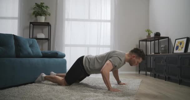 Домашняя тренировка в квартире, атлетичный мужчина делает отжимания в гостиной на ковре, здоровый образ жизни и фитнес, поддерживая форму — стоковое видео