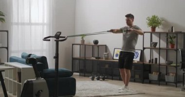 Vücut geliştirici dairede lastik bantlarla antrenman yapıyor, sporcular için güç egzersizi, tecrit ve tecrit süresince ev sağlığı.