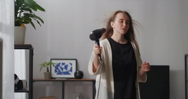 Jovem mulher esbelta está secando o cabelo por secador de cabelo no quarto, soprando ar quente em suas longas fechaduras — Vídeo de Stock