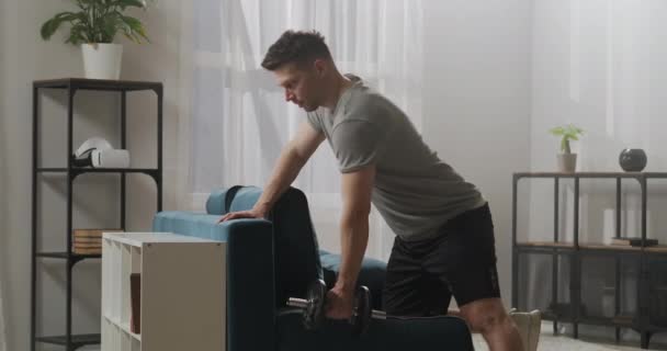 Bodybuilding och hemmaträning, mannen lyfter hanteln i vardagsrummet, tränar i lägenhet, håller formen — Stockvideo