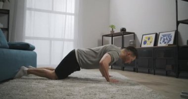 Oturma odasında şınav çeken genç sporcu vücudunun üst kısımları için egzersiz yapıyor. Dairede tek başına antrenman yapıyor, kaslarını geriyor.