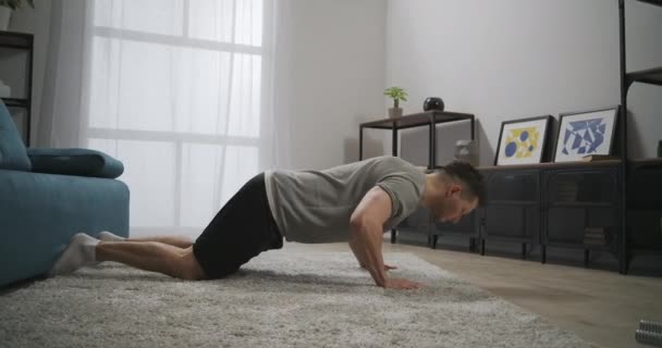 Push-ups στο σαλόνι, νεαρός αθλητικός άνθρωπος κάνει ασκήσεις για το πάνω μέρος του σώματος, προπόνηση μόνο στο διαμέρισμα, τεντώνοντας τους μυς — Αρχείο Βίντεο