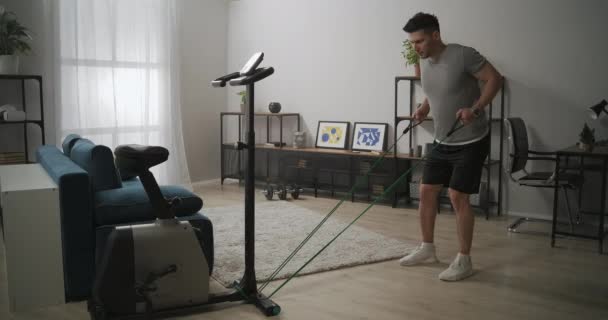 Homme s'entraîne avec élastique à la maison, entraînement de musculation avec équipement sportif dans l'appartement, fitness domestique — Video