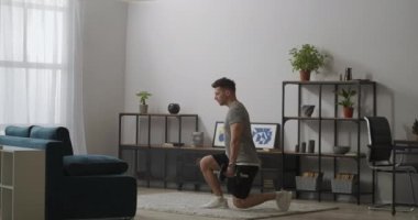 Yakışıklı adam evde tek başına spor yapıyor. Elinde dambıllarla evde oturuyor. Spor, sağlık, fiziksel aktivite.
