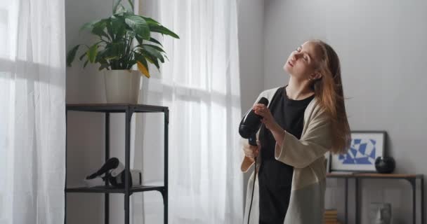 헤어 드라이어를 가진 아름다운 예술 여성이 거실에서 노래를 부르고 있습니다. 근심없고 명랑 한 젊은 여성의 초상화, 감정적 인 얼굴 — 비디오