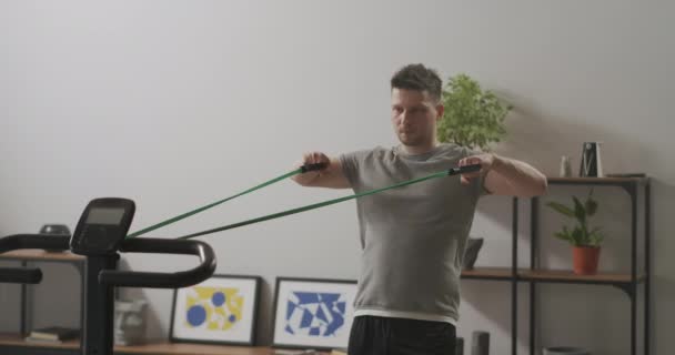 Knappe man doet oefeningen met sport elastiekje in appartement, stretching tape en spannen spieren — Stockvideo