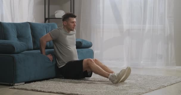 Fitness w domu młody sportowiec, osoba podnosi swoją wagę opierając się na kanapie w salonie — Wideo stockowe
