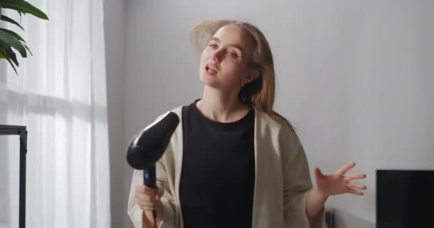 Csinos éneklő nő hajszárítóval a nappaliban, portré beltérben, gondtalan és örömteli arc fiatal hölgy — Stock videók
