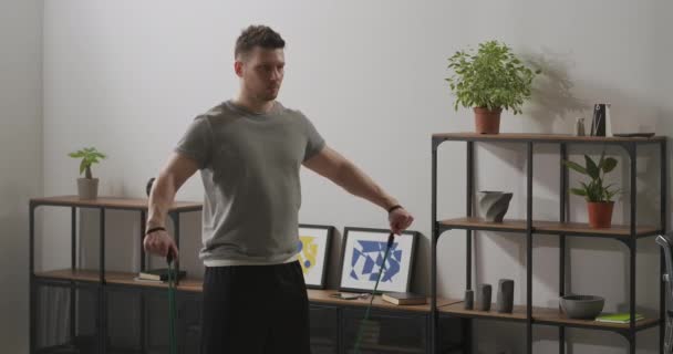 Homem desportivo bonito está fazendo treino em casa, usando elásticos elásticos para treinar braços e ombros — Vídeo de Stock