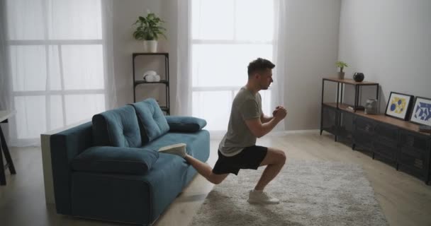 Sexy Mann macht körperliche Bewegung im Wohnzimmer, Kniebeugen für starke Beinmuskeln, Heimfitness und Workout — Stockvideo