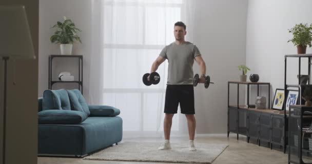 Сильный человек тренируется дома во время самоизоляции, поднимая гантели, силовые тренировки для хорошей формы тела — стоковое видео