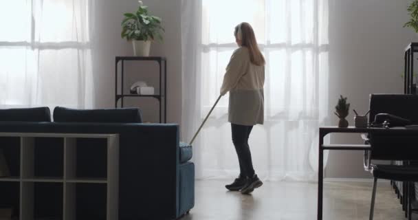 Deveres domésticos e tarefas domésticas, mulher jovem está cantando para esfregar durante a lavagem do chão no apartamento, bom humor positivo e — Vídeo de Stock