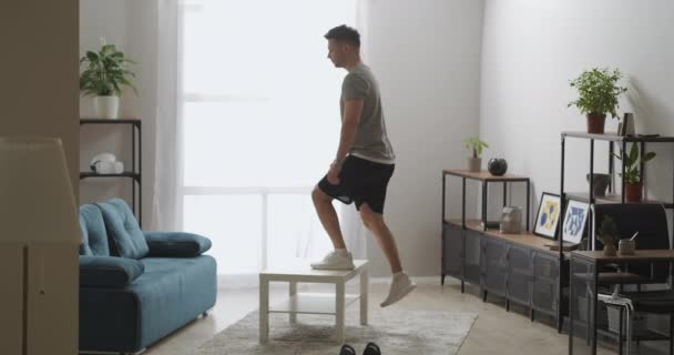 Activité physique dans la salle de gym à domicile, l'homme utilise une table comme un équipement sportif, levant et abaissant, musculation des jambes d'entraînement — Video