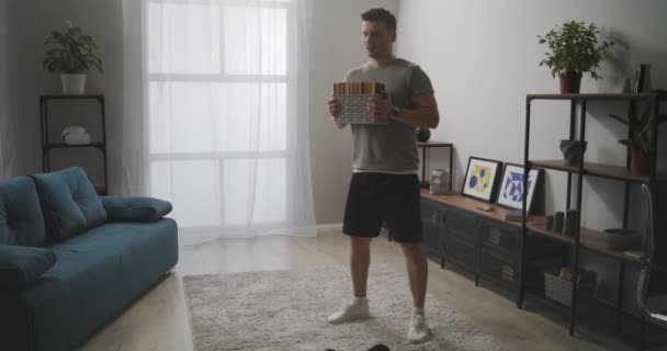 Тренируясь дома, мужчина делает приседания с весом, держит в руках книги, тренируется в квартире для поддержания физической формы — стоковое видео