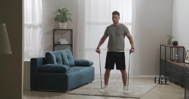 Homem bonito adulto está fazendo exercícios físicos com bandas elásticas em casa, treino de força, mantendo uma boa condição física — Vídeo de Stock