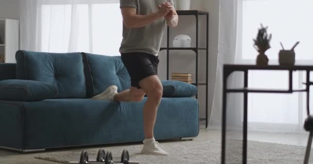 Home gym, jongeman is alleen trainen in de woonkamer in het weekend, doen hurken op een been, spannen spieren van het lichaam — Stockvideo