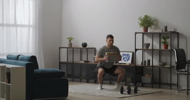 Домашній спортзал для здорового способу життя і підтримки пристосованості, чоловік робить присідання, тримаючи книги в руках, тренування сили — стокове відео