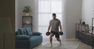 Sporcu dairede çömeliyor, ağırlıkları elinde tutuyor, kaslı seksi vücudu için fiziksel egzersiz yapıyor, vücut geliştiriyor.