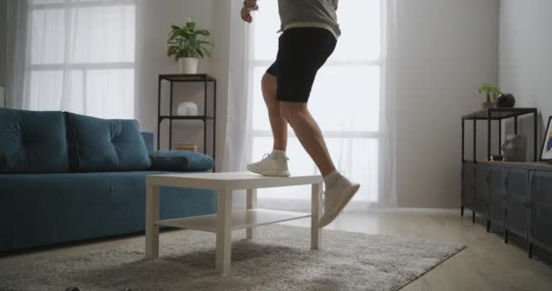 Homme athlétique s'entraîne avec table dans l'appartement, faire de l'exercice pour les muscles des jambes, meubles comme l'équipement sportif à la maison, mode de vie sain — Video